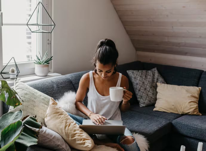 Femme avec une tasse assise sur un canapé avec un ordinateur portable